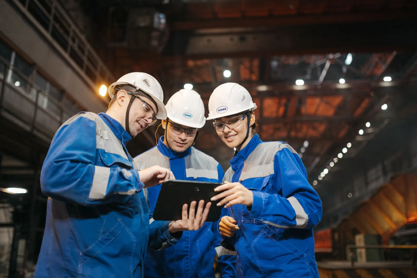 Engenheiros com equipamento de proteção analisam indicadores em um tablet dentro de uma planta industrial